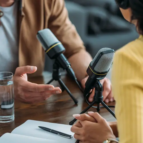 Two podcasters sitting at a table with microphones and notes in a studio near Nolensville, TN at The Podcast Pod in Brentwood